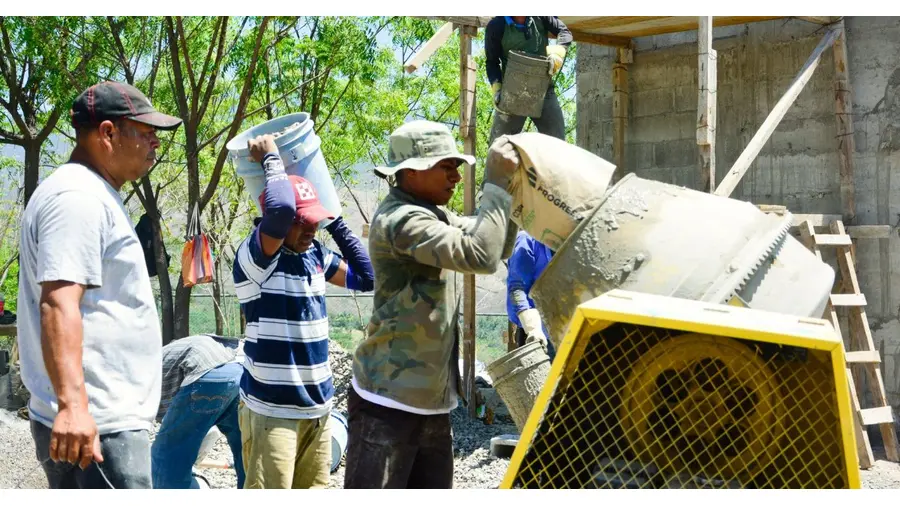 Outdoor construction site with workers pouring cement from mixers and buckets.