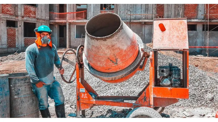 A construction worker operating a concrete mixer at an active building site, emphasizing safety gear.