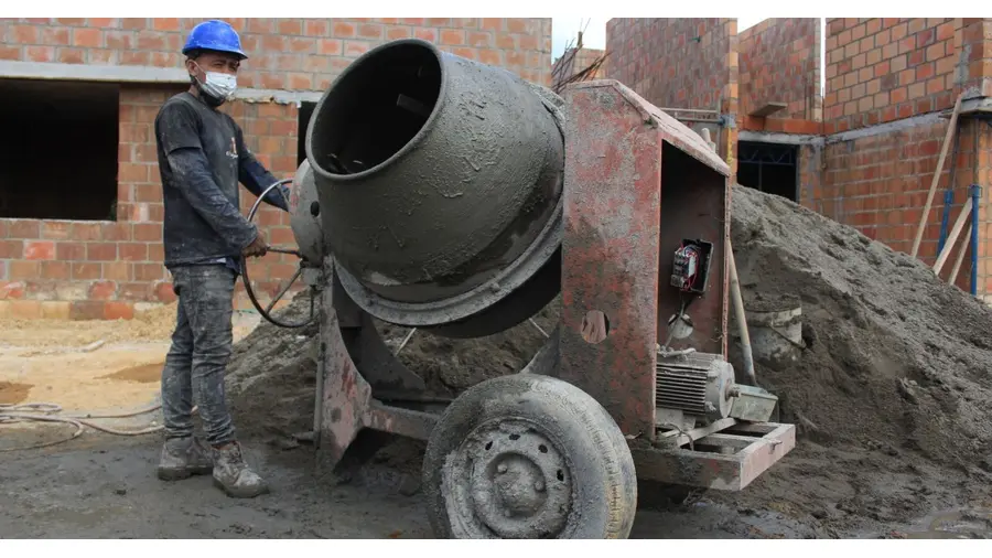 A construction worker in safety gear operates a cement mixer at a building site.