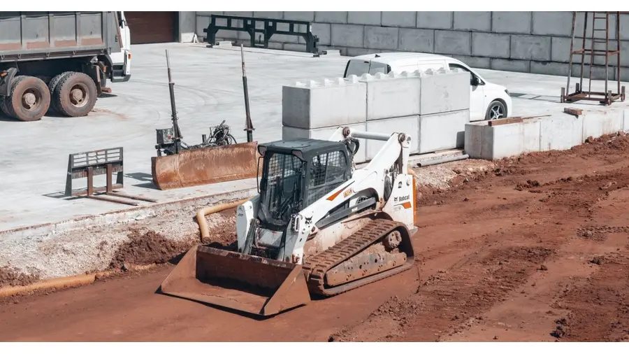 Bulldozer working on a construction site alongside a white truck and concrete blocks.