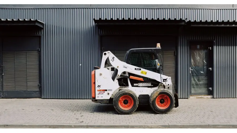 Small white truck loader parked on sidewalk near entrance of modern warehouse on street in city