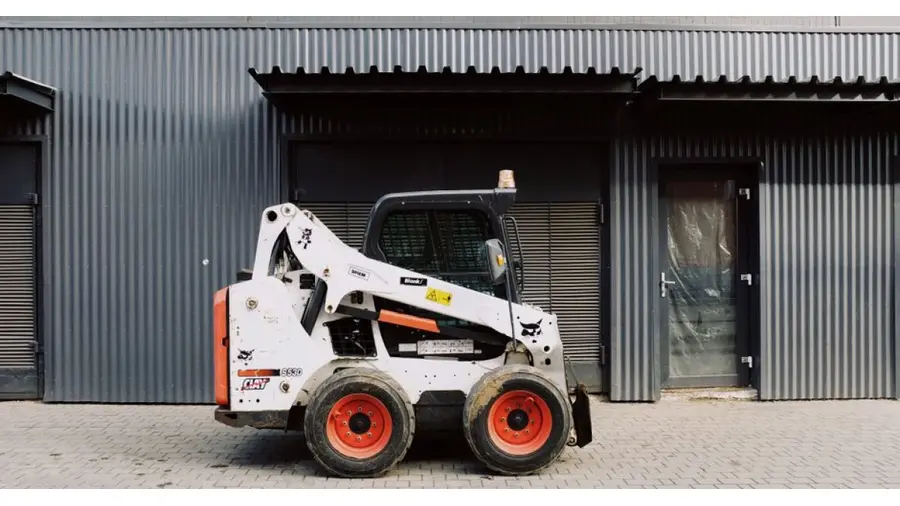 Small white truck loader parked on pavement near black wall of modern building on street in city