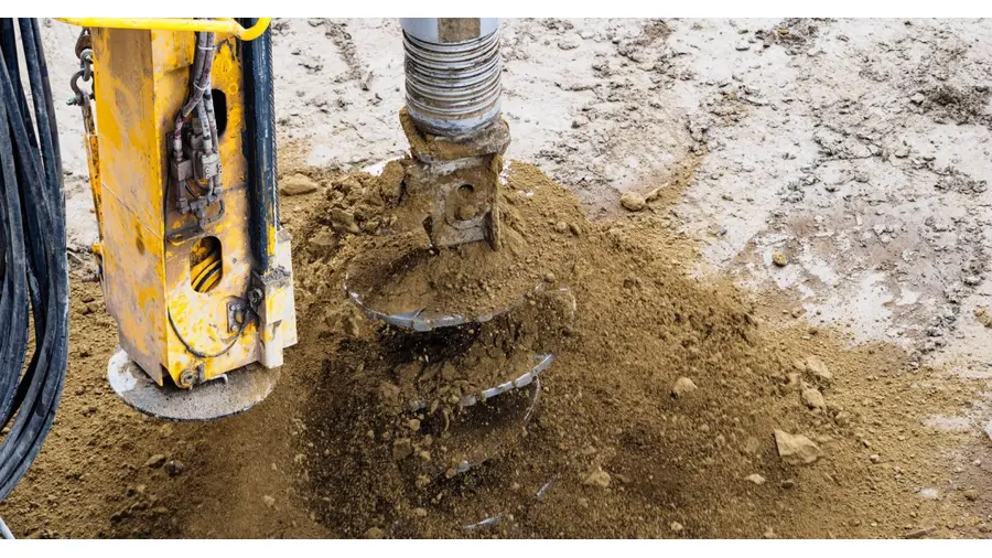 A close-up of a powerful drilling machine working on soil at a construction site.