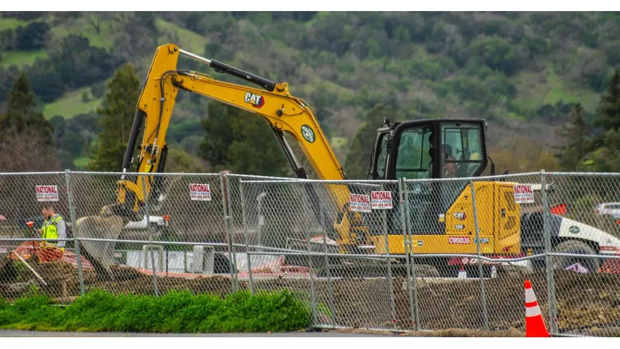 Excavator working at a construction site with safety fences and workers, depicting industry work environment.