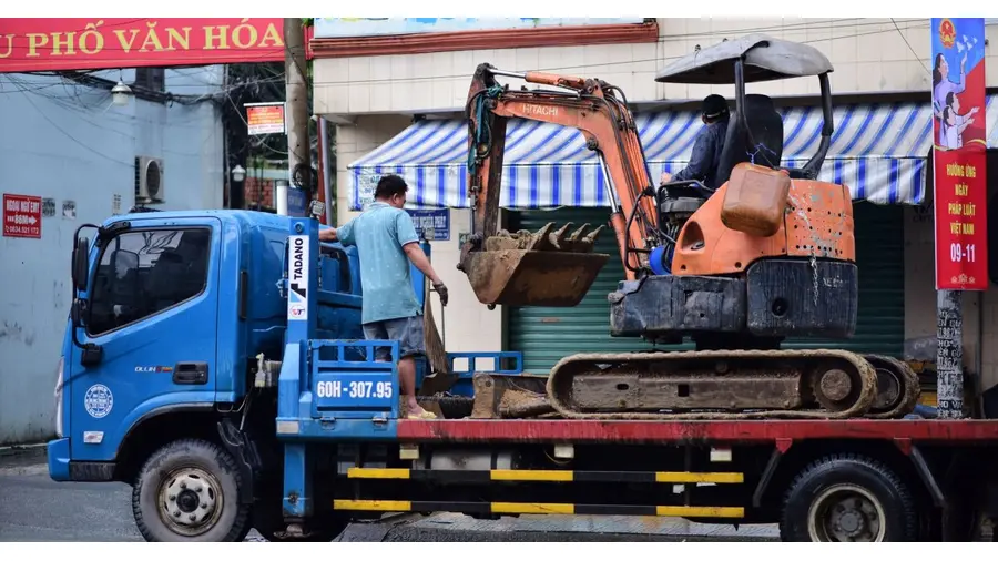 Excavator being loaded onto a truck in a busy urban street, showcasing construction work.